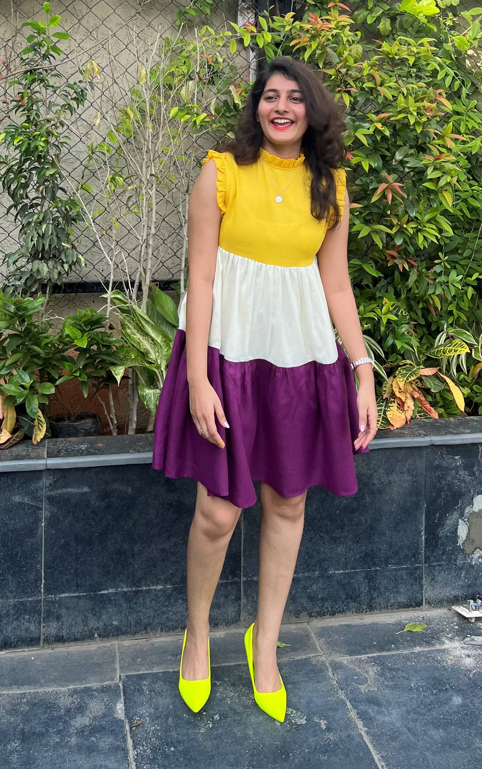 Pallavi stands and smiles in a colorful dress with bushes in the background